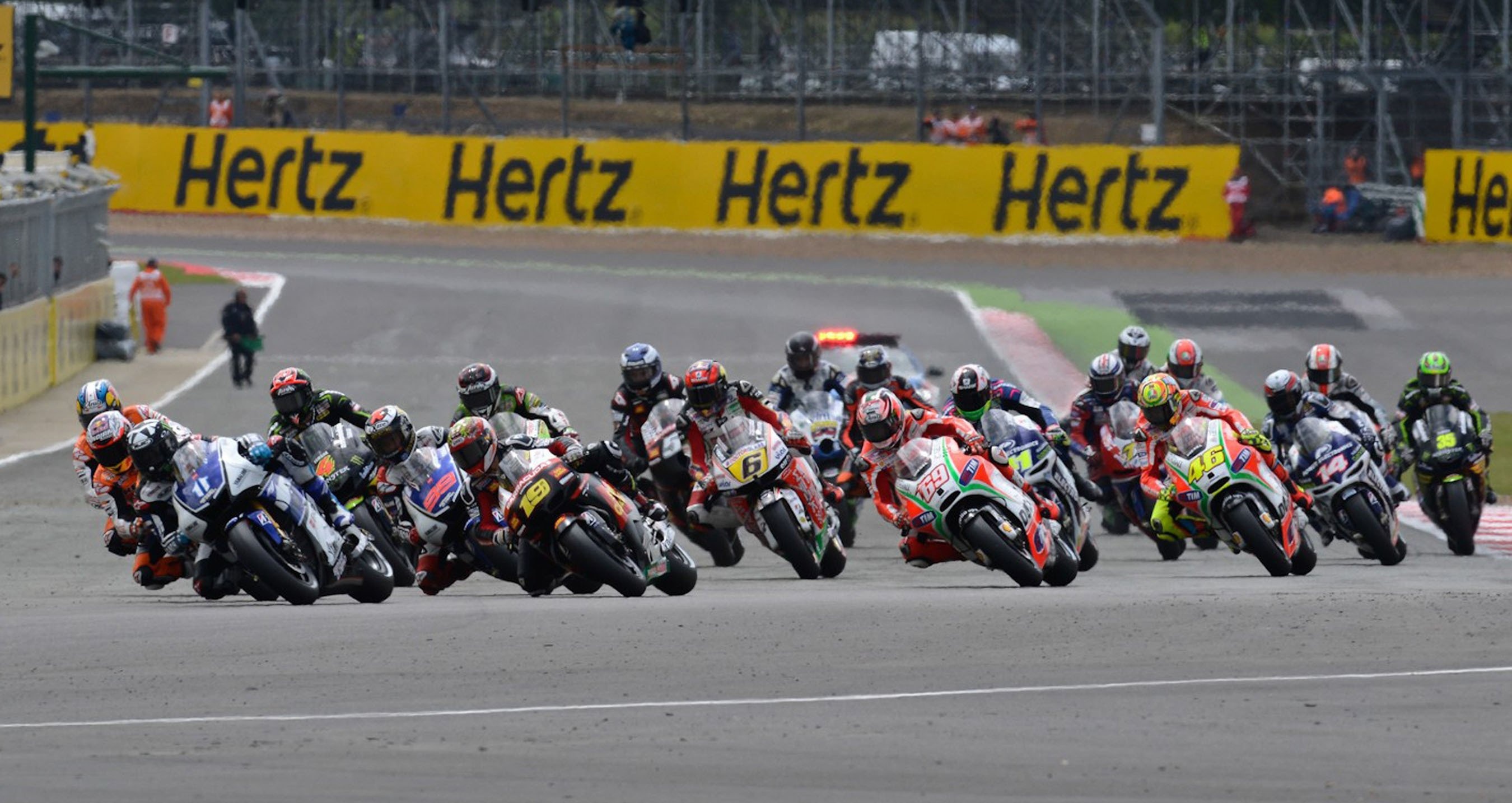MotoGP pack first corner, Riders leaning in formation, Yellow trackside hoardings, HD Desktop wallpaper