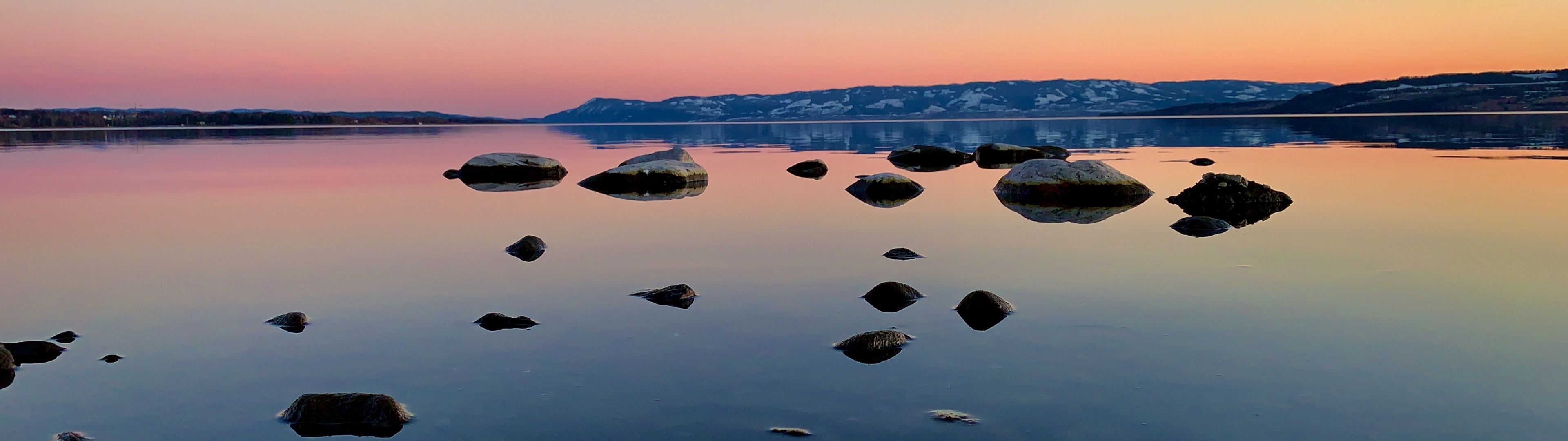 submerged smooth lake boulders, distant snow-dusted hills, pink twilight dusk sky, Dual Screen Desktop wallpaper