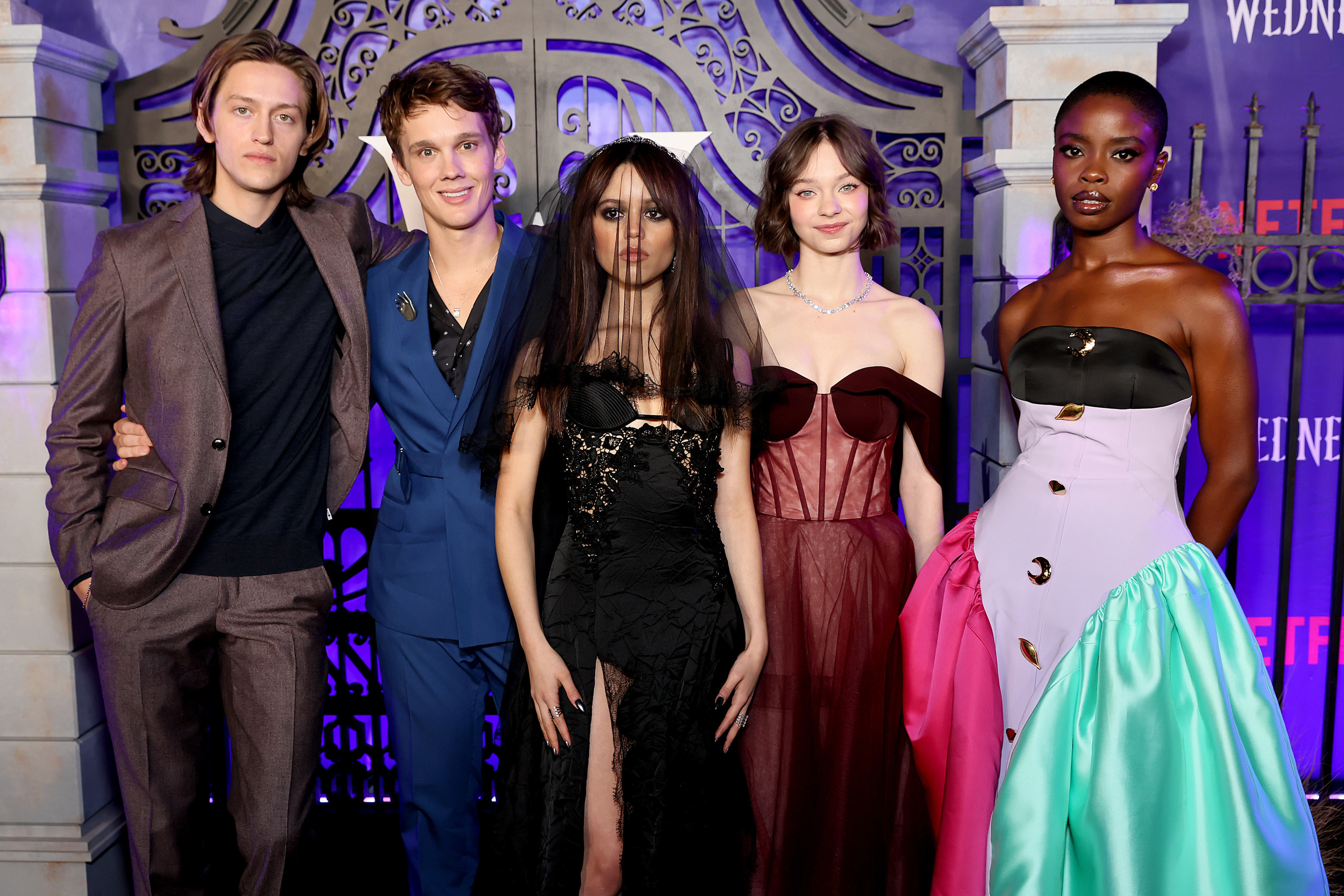 Emma Myers in maroon gown, Jenna Ortega in black lace gown, Wednesday premiere cast lineup, Purple gothic gate backdrop, HD Desktop wallpaper