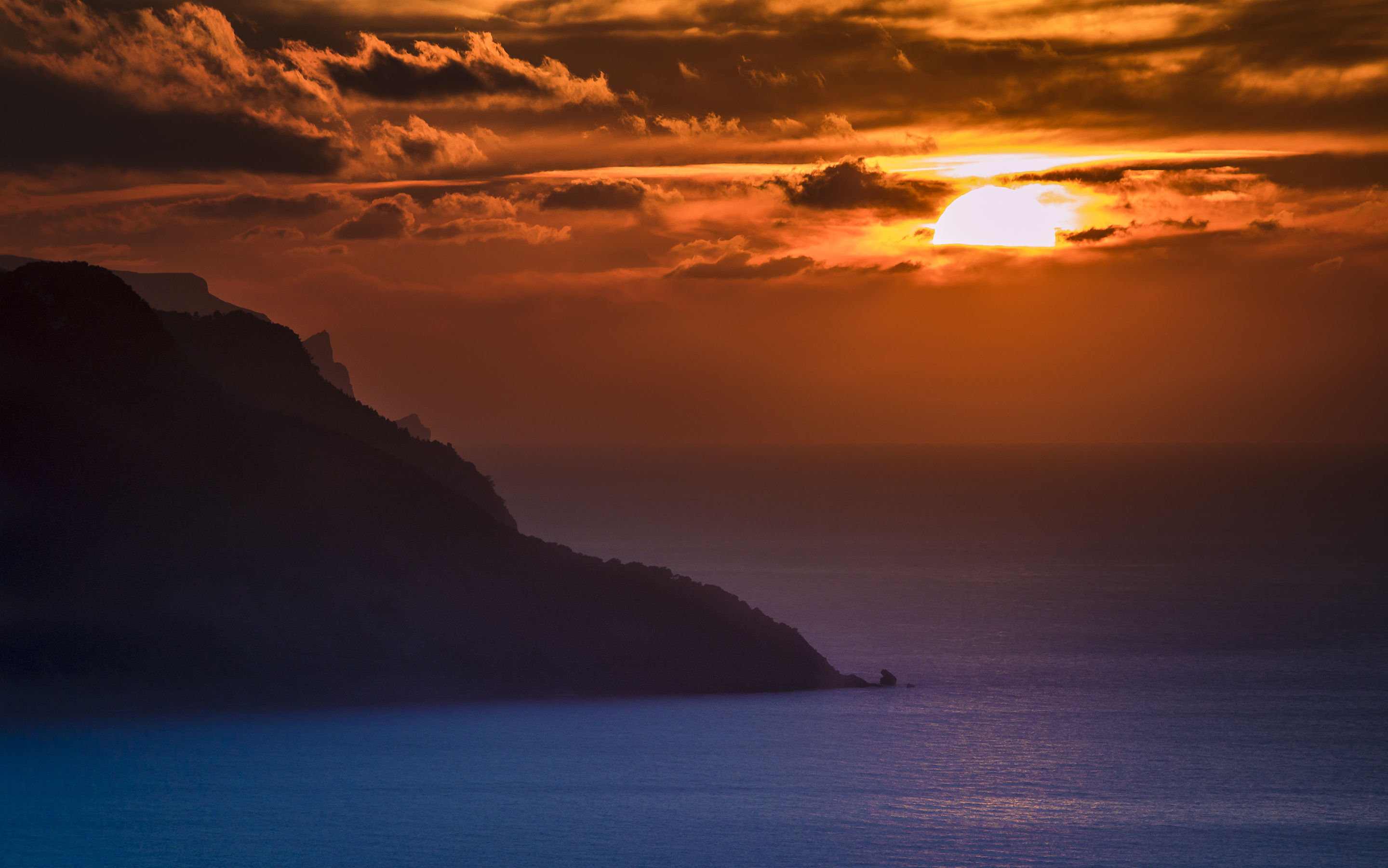 Golden sun behind clouds, Silhouetted coastal headland ridge, Deep blue ocean waters, HD Desktop wallpaper