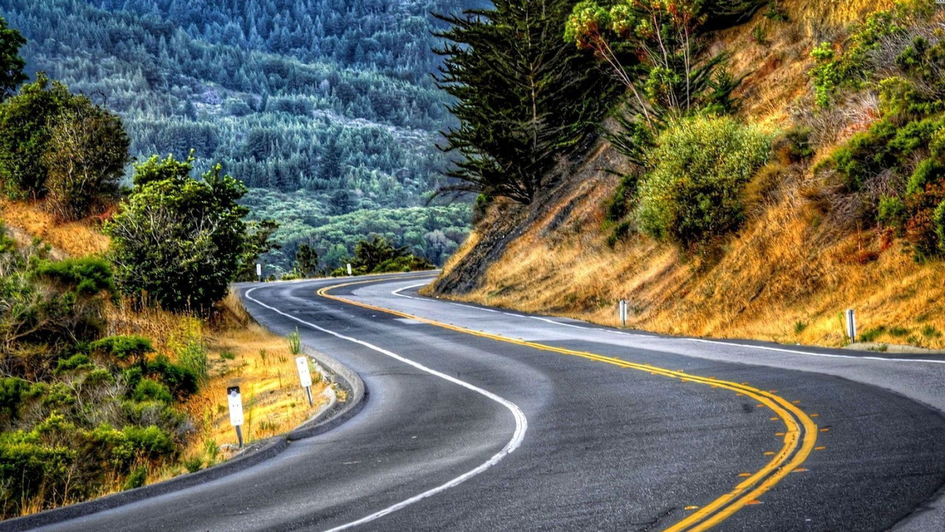 winding two-lane mountain highway, double yellow center lines, conifer-covered mountain slope, Full HD Desktop wallpaper