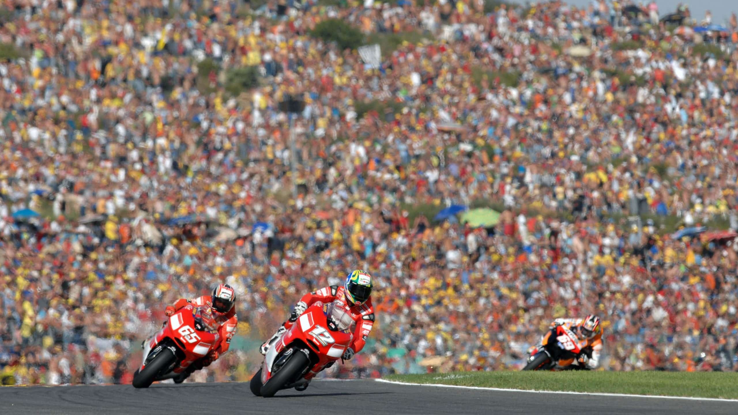Troy Bayliss number 12, Loris Capirossi number 65, Repsol Honda rider behind, Packed grandstand crowd, MotoGP pack over crest, HD Desktop wallpaper