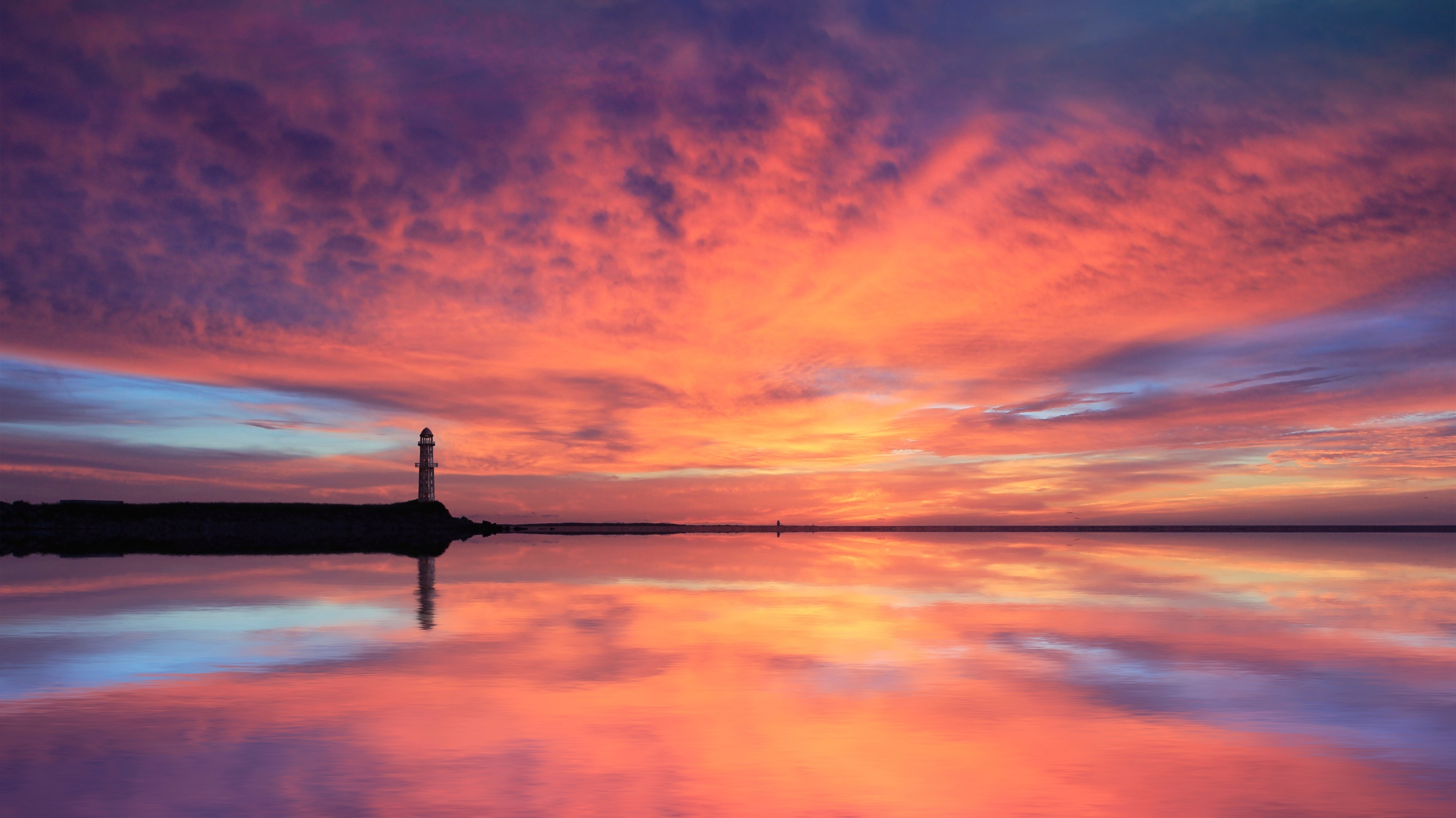 silhouetted coastal lighthouse, vibrant orange dusk sky, calm water mirror reflection, 4K Desktop wallpaper