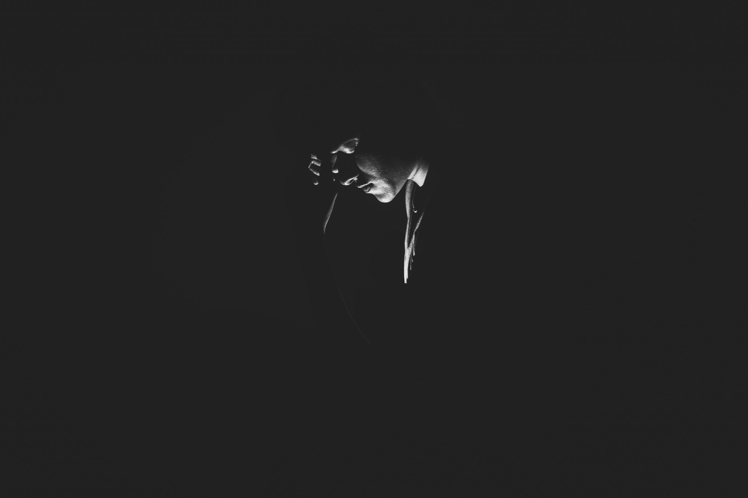 Person with bowed head, High-contrast chiaroscuro lighting, Minimalist black negative space, HD Desktop wallpaper