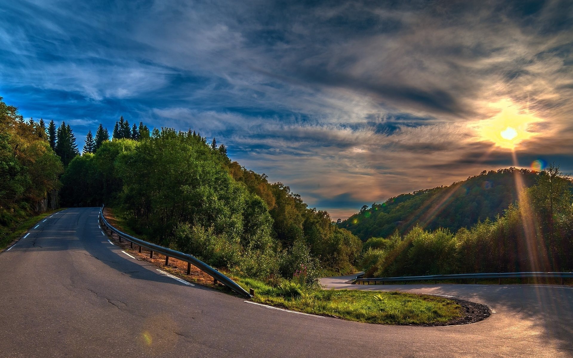 winding asphalt switchback road, sunburst over forested hills, curved metal guardrail, HD Desktop wallpaper