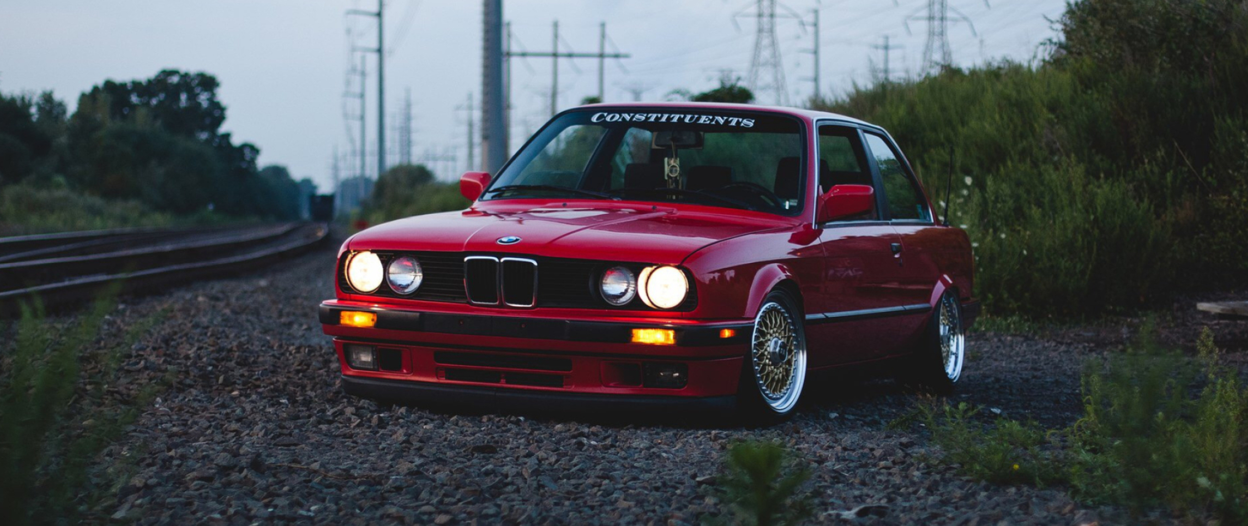red BMW E30 coupe, CONSTITUENTS windshield banner, gravel railroad tracks, Dual Screen Desktop wallpaper
