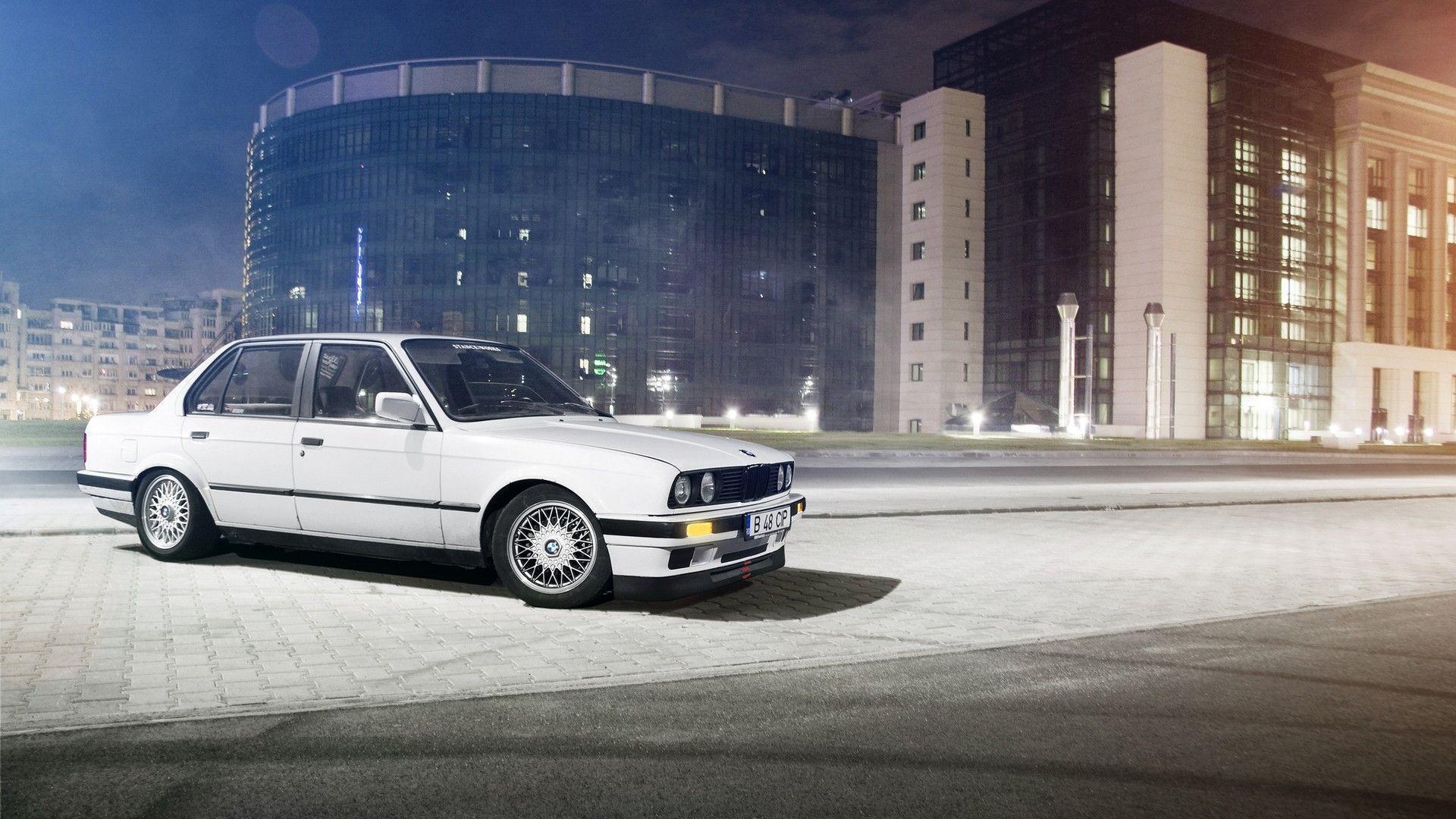 white BMW E30 sedan, cross-spoke mesh wheels, illuminated modern city building, Full HD Desktop wallpaper