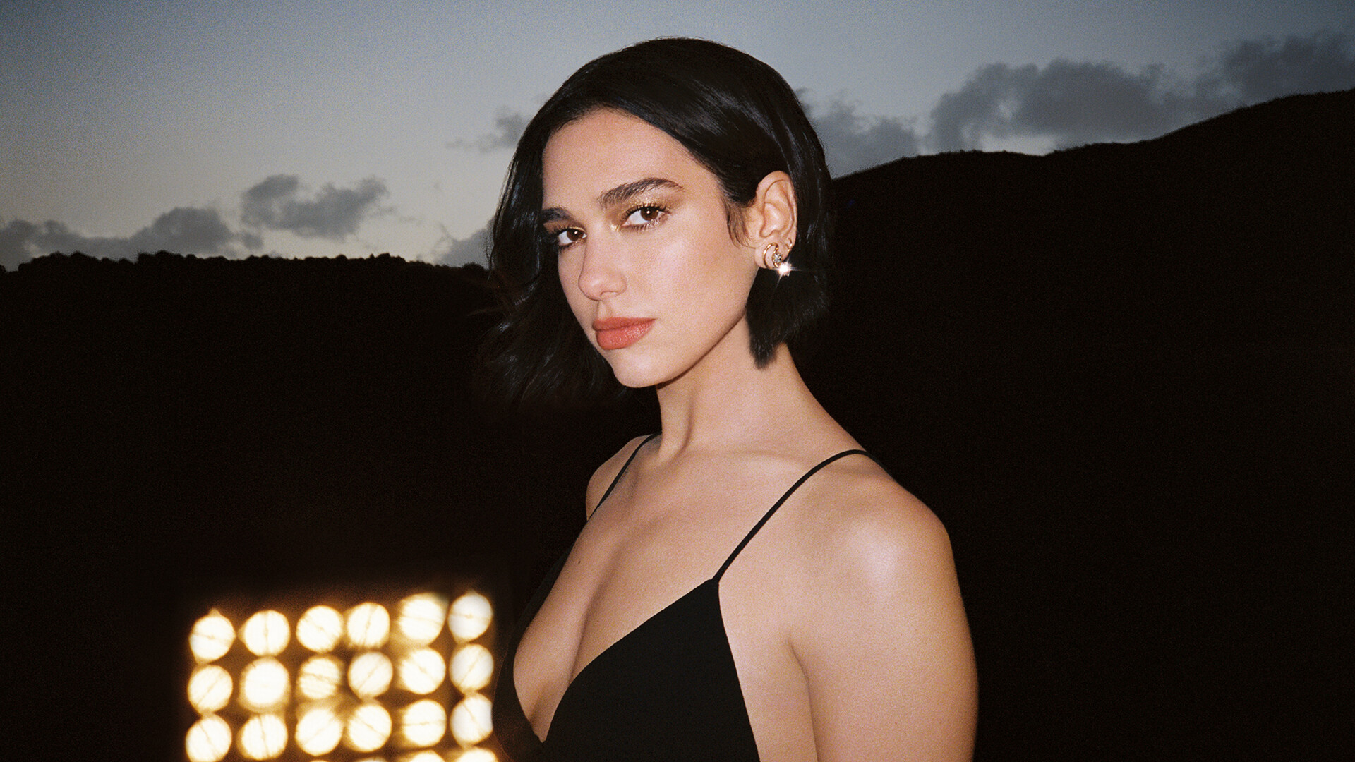 Dua Lipa, Twilight outdoor portrait, Black camisole, Glowing floodlight bank, Full HD Desktop wallpaper