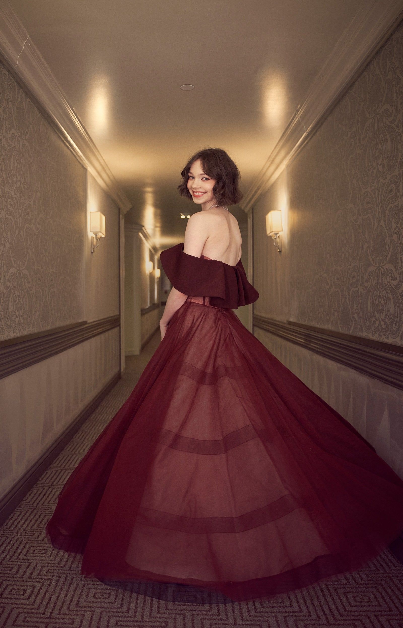 Emma Myers in burgundy ball gown, Off-shoulder tulle skirt, Hotel corridor with wall sconces, HD Phone wallpaper