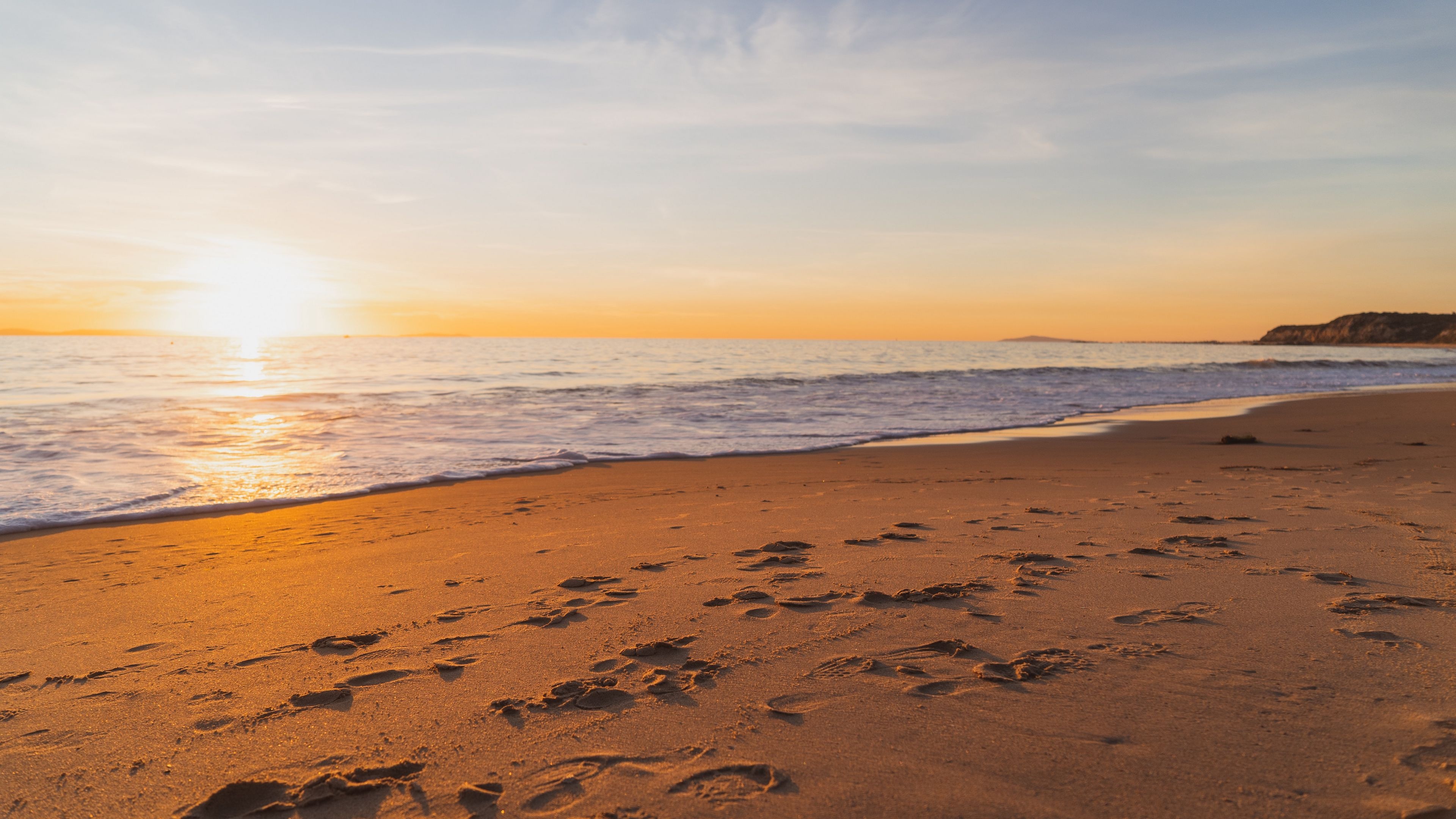 footprints in beach sand, gentle breaking ocean surf, golden hour ocean sunset, 4K Desktop wallpaper