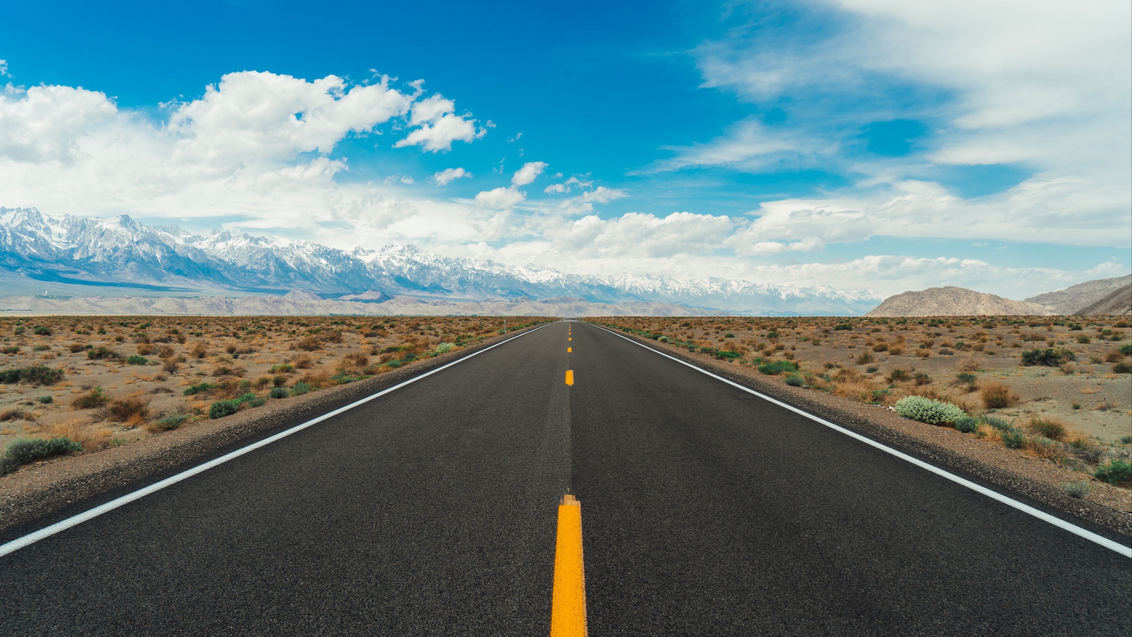 snowcapped Sierra Nevada mountains, straight asphalt highway, arid desert scrubland, 4K Desktop wallpaper