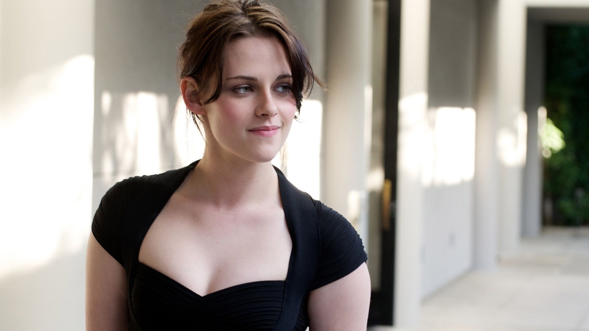 Kristen Stewart, black cap-sleeve dress, sunlit architectural corridor, Full HD Desktop wallpaper